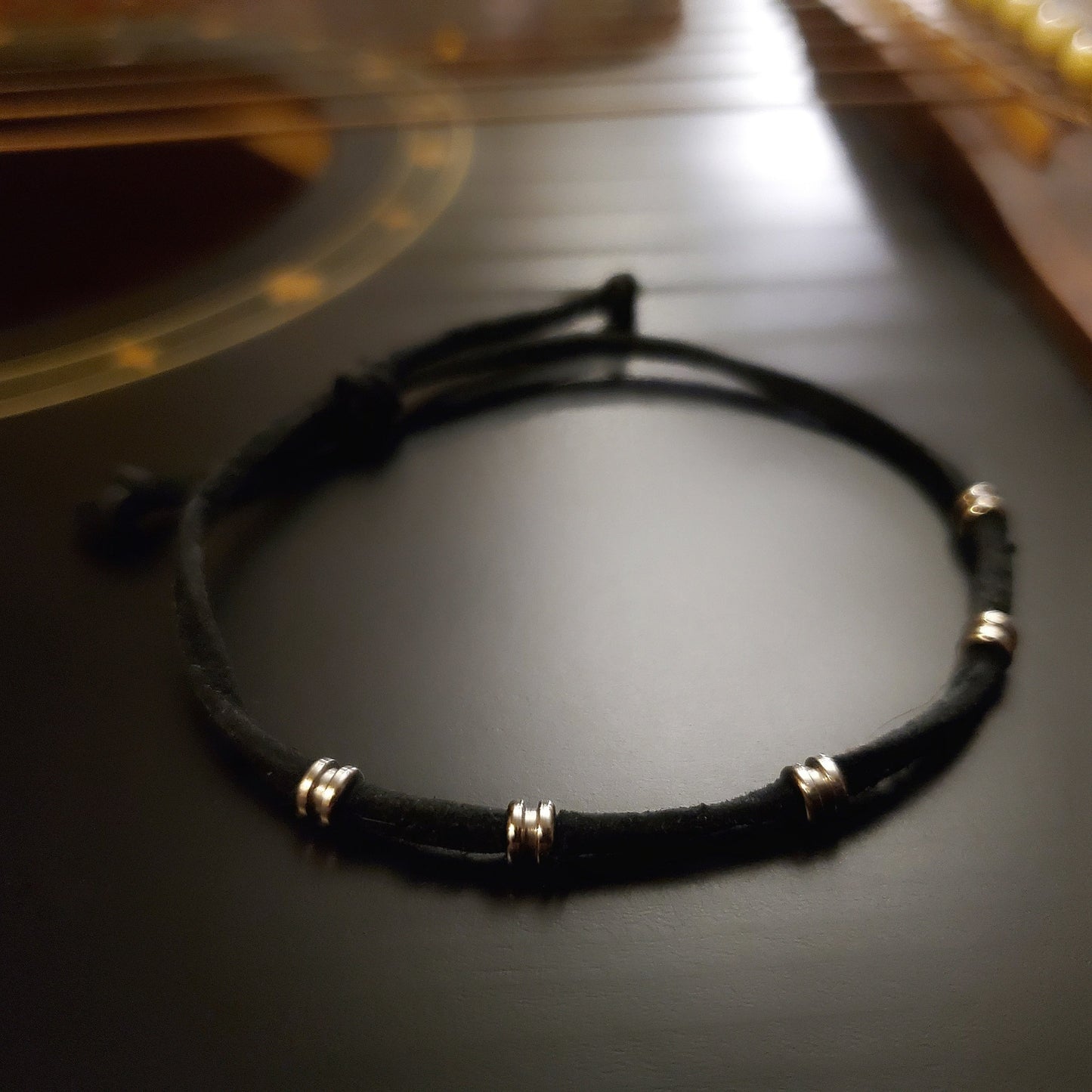 black bracelet made from a suede cord and silver coloured guitar string ballends sitting on the body of a black guitar