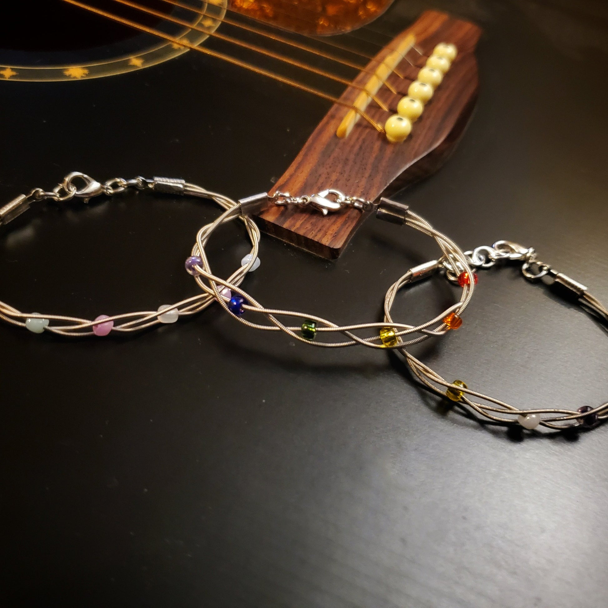 three clasp style bracelet made from braided upcycled guitar strings with glass beads representing the LGBTQ/Trans/Non-Binary Pride flags