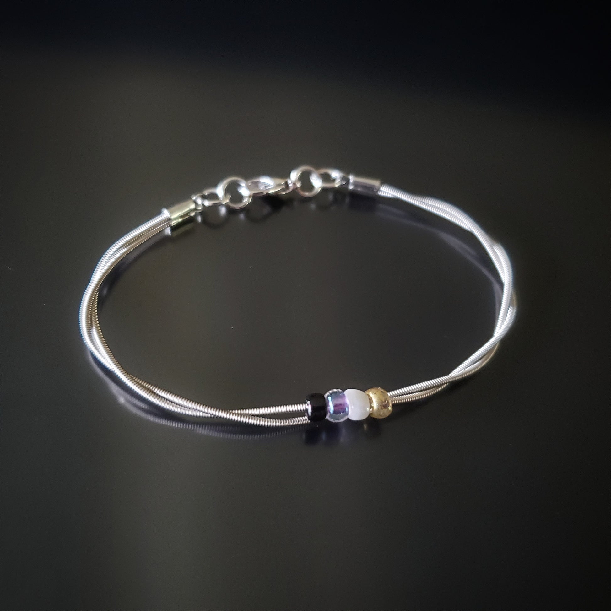 silver coloures clasp style bracelet with 4 glass beads representing the non-binary flag (yellow, white, purple & black) 