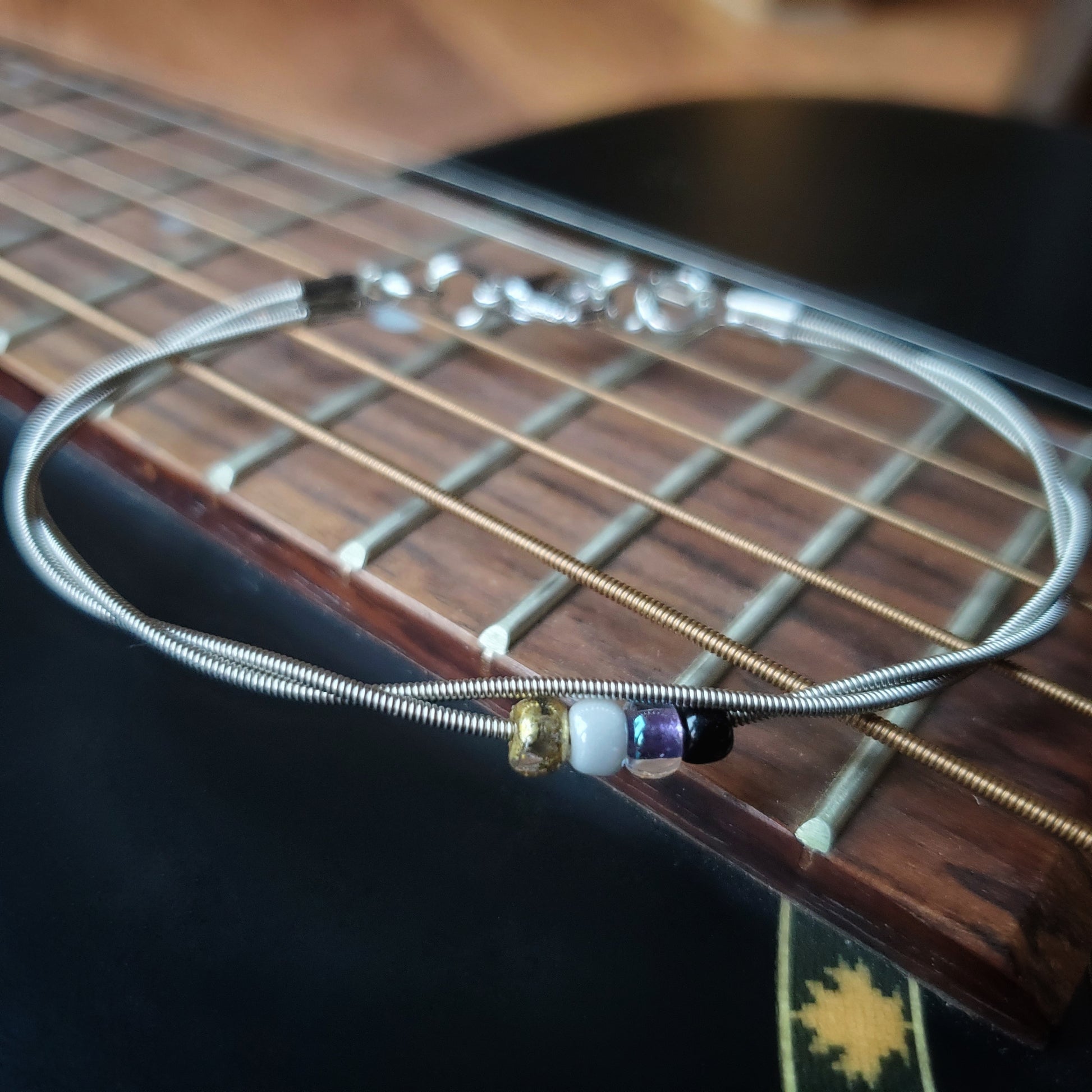silver coloures clasp style bracelet with 4 glass beads representing the non-binary flag (yellow, white, purple & black) -bracelet is on a black guitar