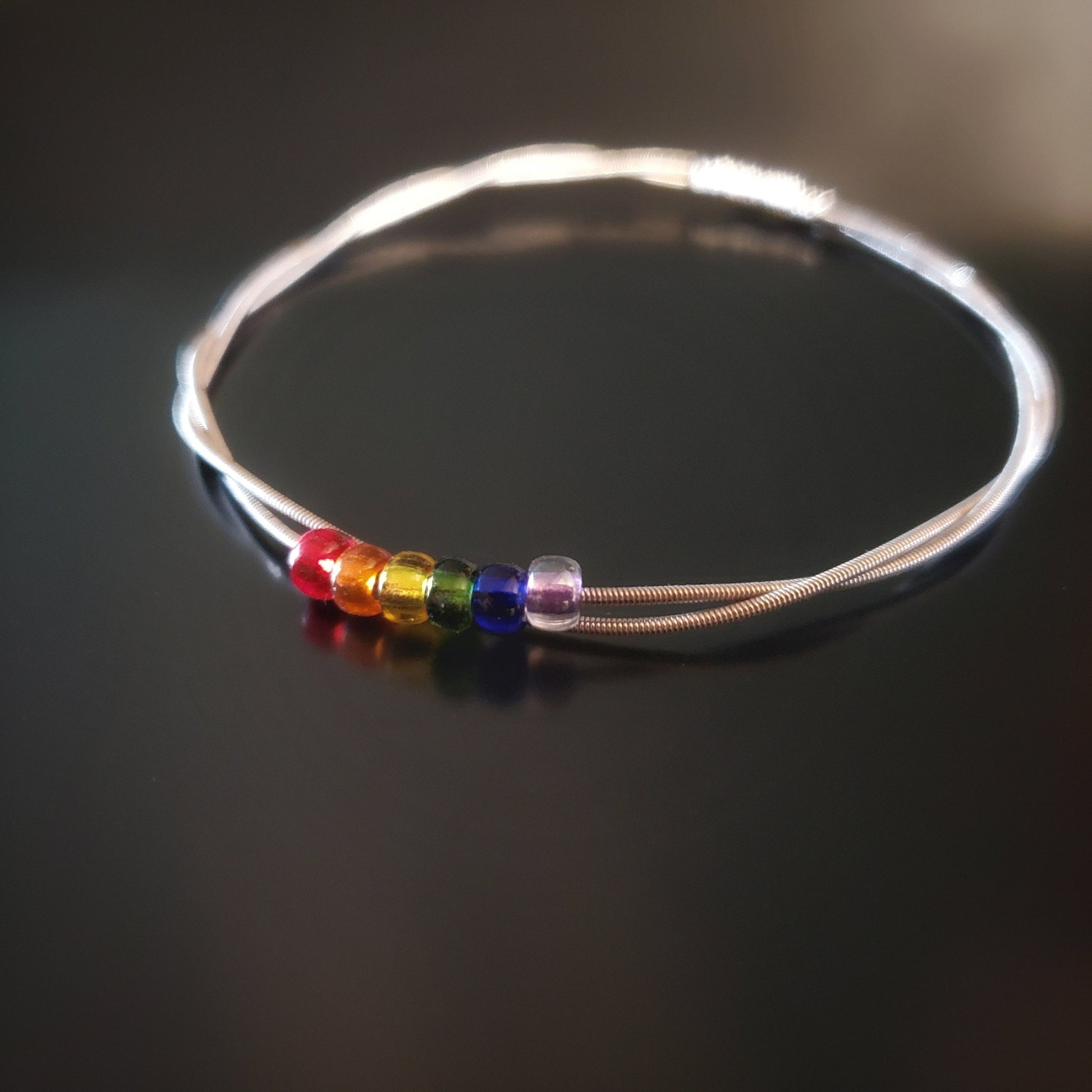 bangle style bracelet made from an upcycled guitar string - 6 glass beads represent the colours of the LGBTQ flag (red, orange, yellow, green, blue and purple)