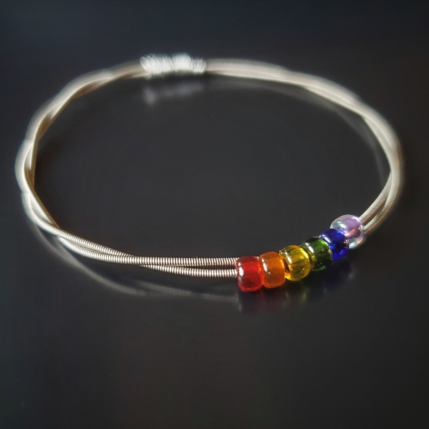 bangle style bracelet made from an upcycled guitar string - 6 glass beads represent the colours of the LGBTQ flag (red, orange, yellow, green, blue and purple)