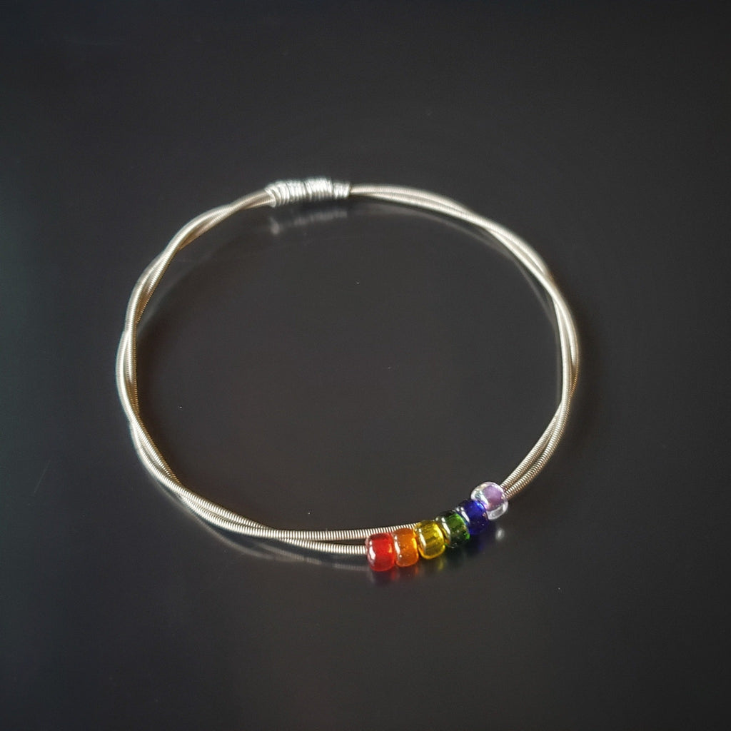 bangle style bracelet made from an upcycled guitar string - 6 glass beads represent the colours of the LGBTQ flag (red, orange, yellow, green, blue and purple)