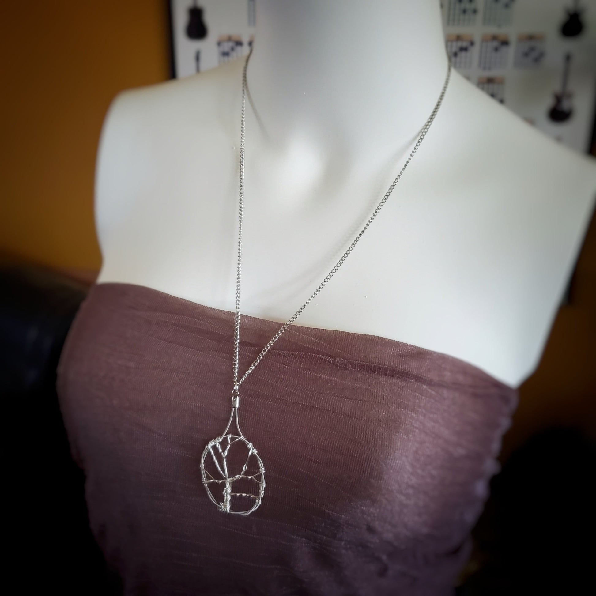white woman's bust wearing a a necklace made with a chain on which hangs a pendant in the shape of a tree with a circle around it - the tree is made of silver coloured wire and the circle is made from upcycled guitar strings 