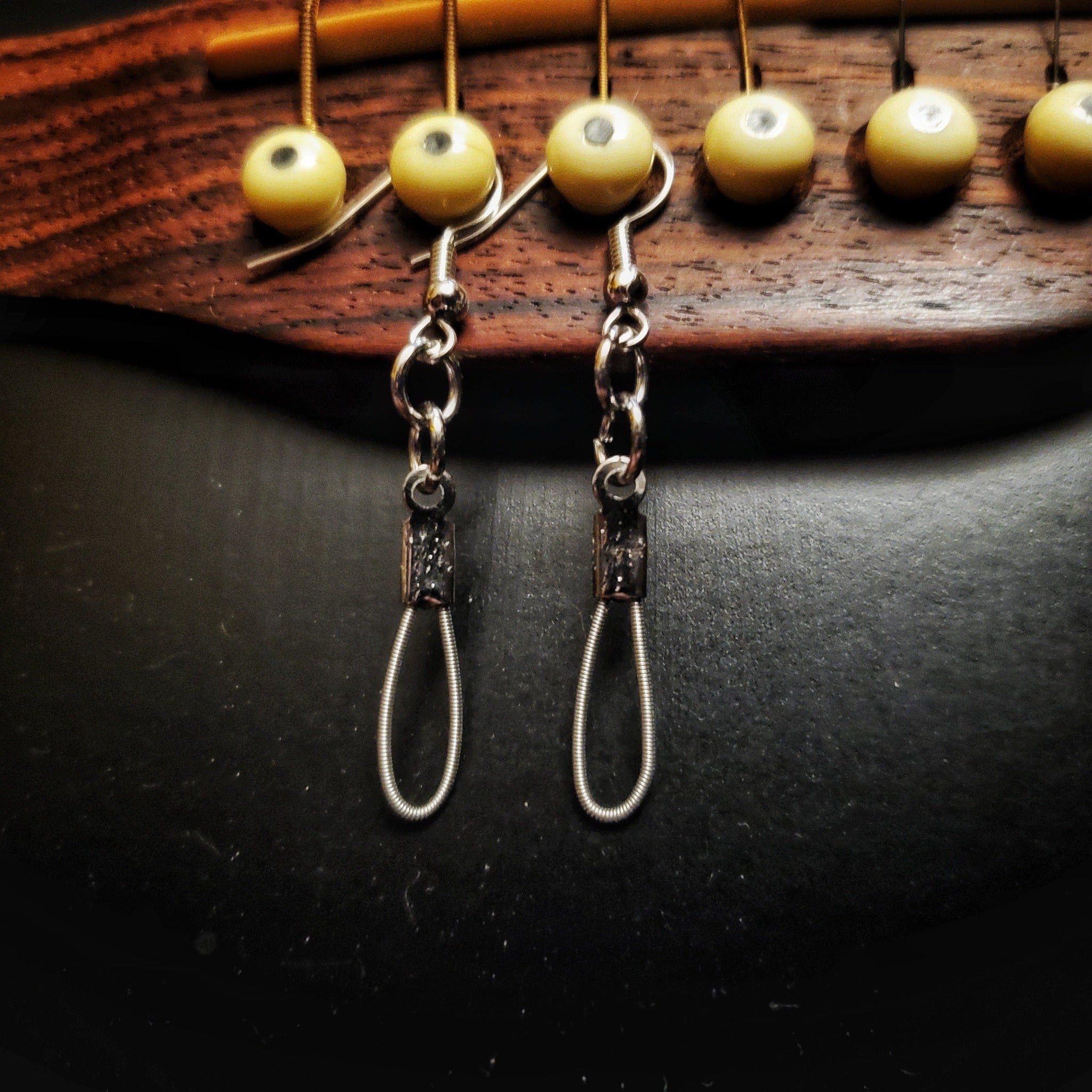 small teardrop style earrings made from upcycled guitar strings hanging from the bridge of a black guitar