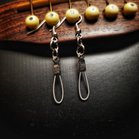small teardrop style earrings made from upcycled guitar strings hanging from the bridge of a black guitar