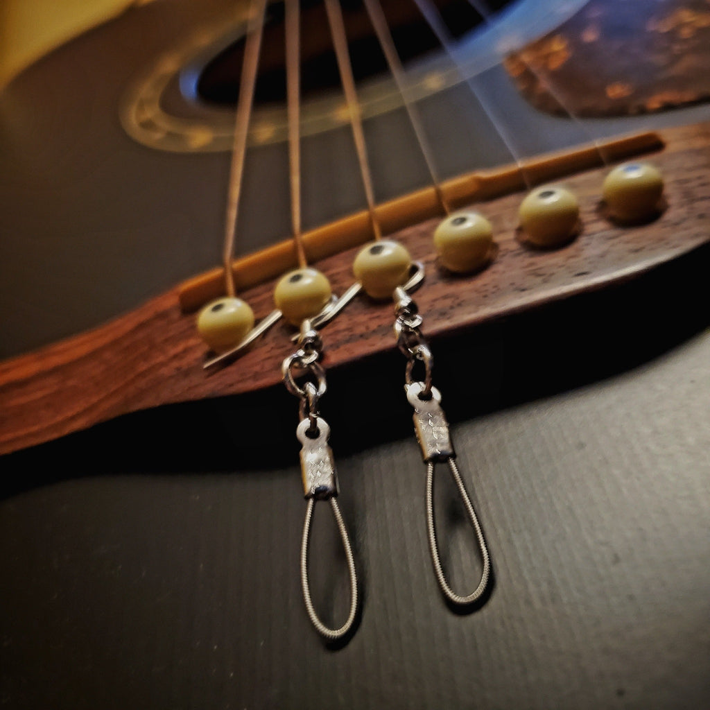 small teardrop style earrings made from upcycled guitar strings hanging from the bridge of a black guitar
