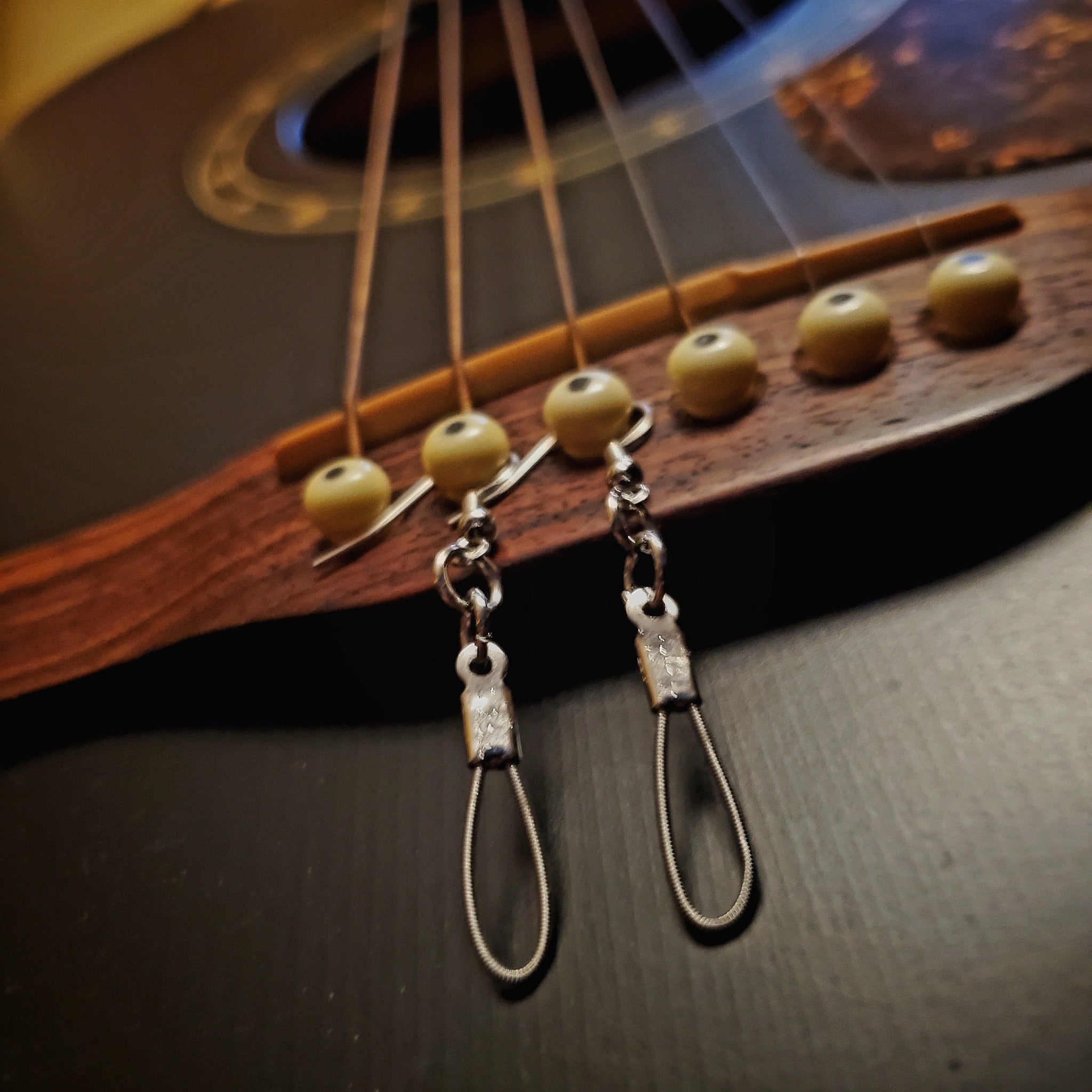 small teardrop style earrings made from upcycled guitar strings hanging from the bridge of a black guitar