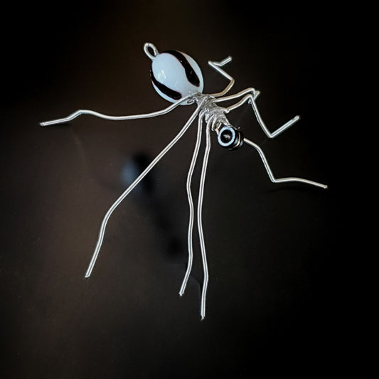 spider sculpture made from silver guitar strings and a black and white bead on a black background