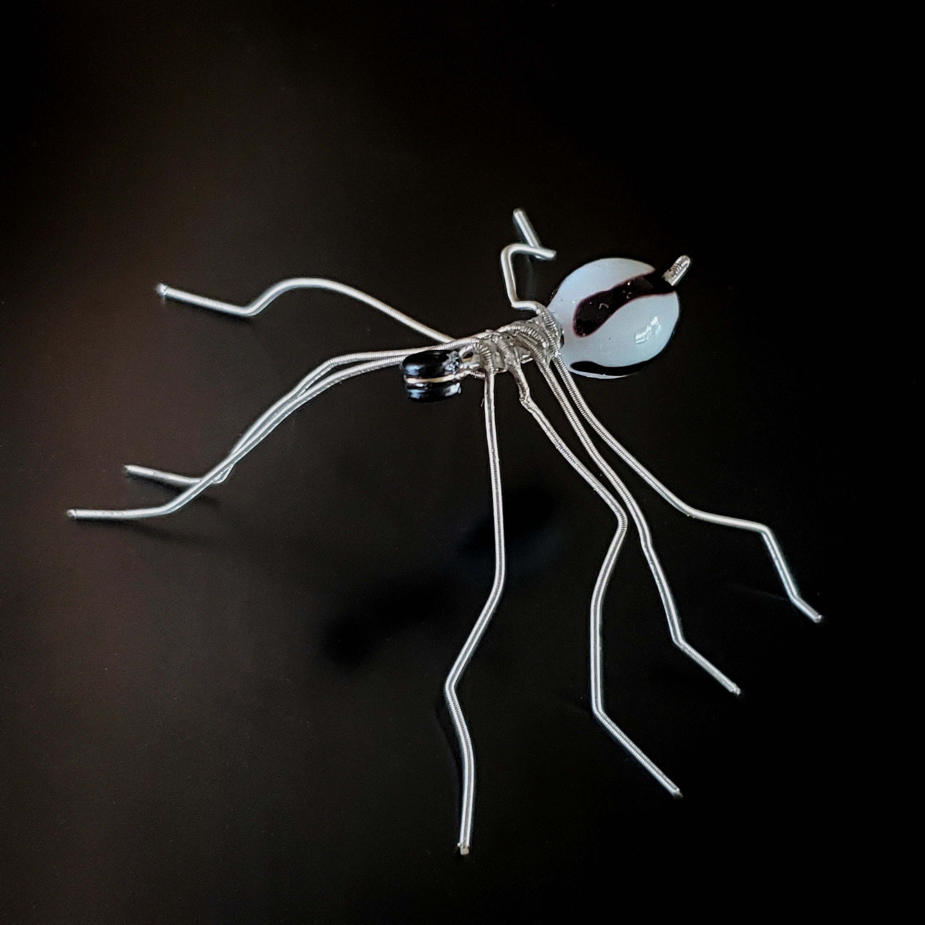 spider sculpture made from silver guitar strings and a black and white bead on a black background