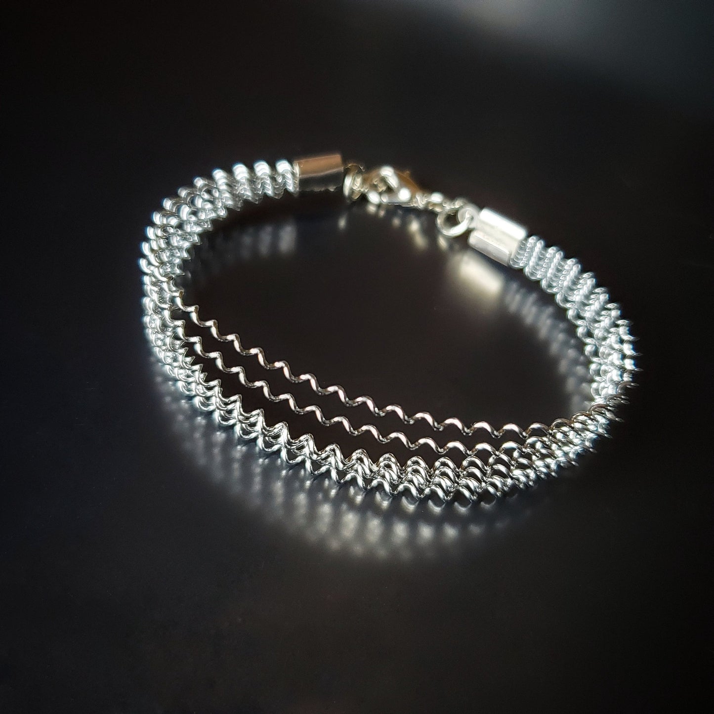 silver coloured clasp style bracelet made from a series of upcycled snare drum strings 