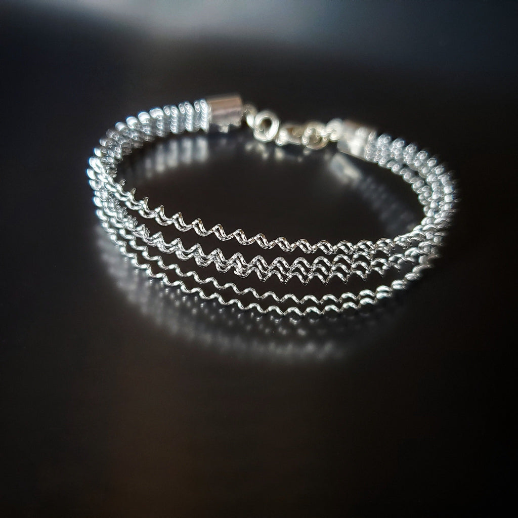 silver coloured clasp style bracelet made from a series of upcycled snare drum strings 