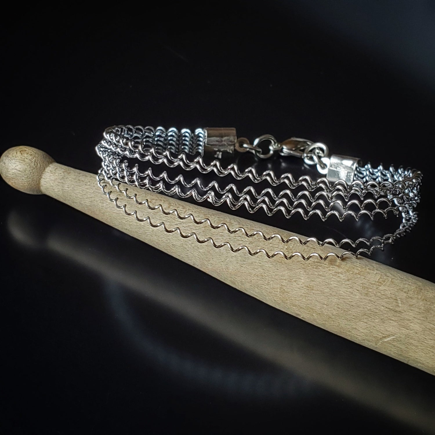 silver coloured clasp style bracelet made from a series of upcycled snare drum strings - bracelet is sitting on a drumstick