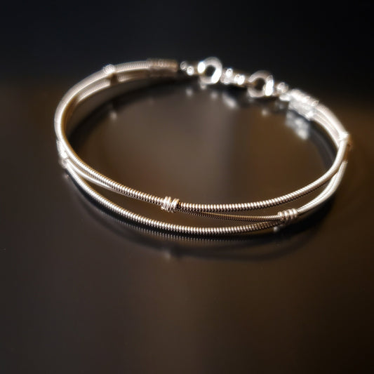clasp style silver coloured bracelet Made from 3 upcycled guitar strings (2 thicker and 1 thinner) the center string is shaped like a wave alternatively touching the top and then the bottom string