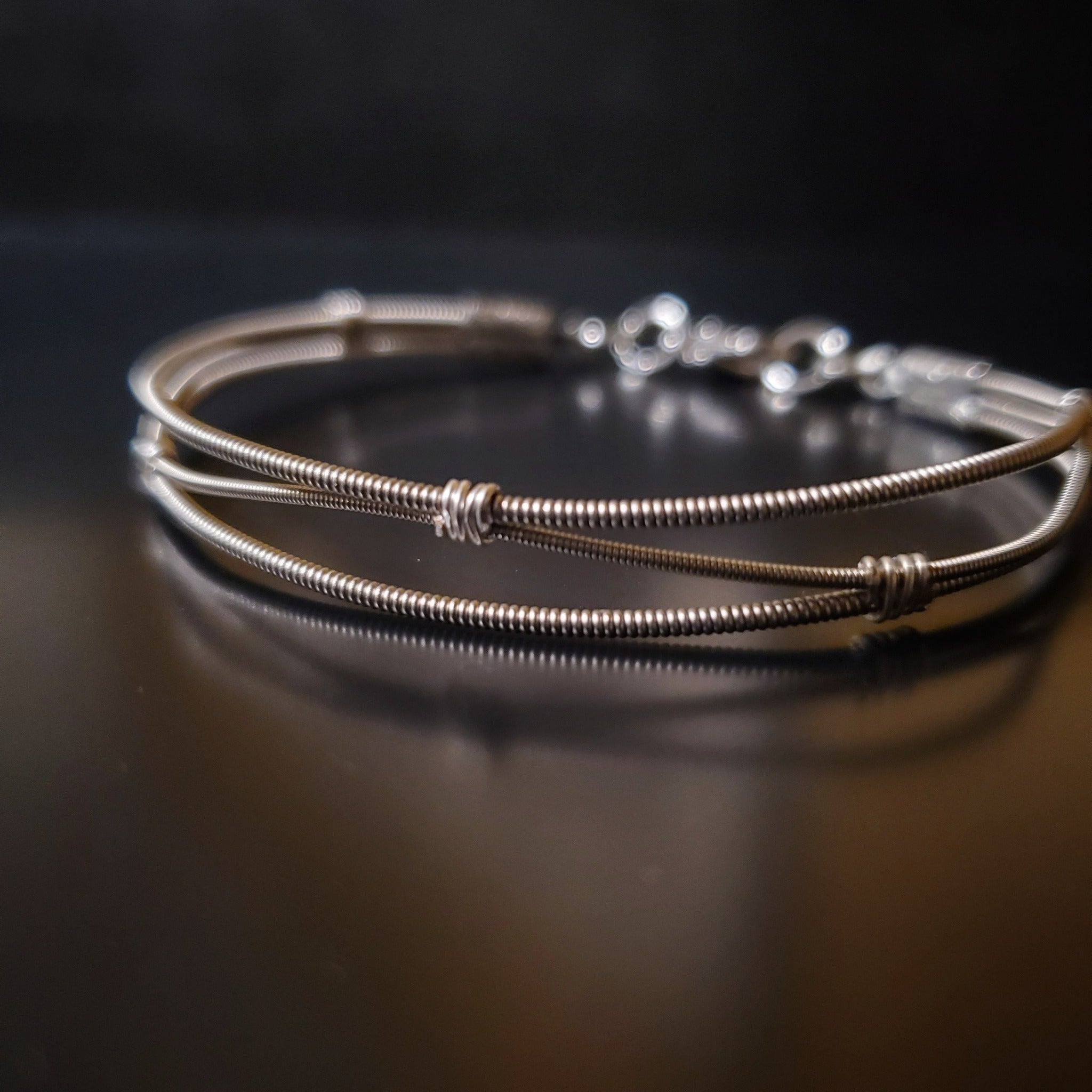 clasp style silver coloured bracelet Made from 3 upcycled guitar strings (2 thicker and 1 thinner) the center string is shaped like a wave alternatively touching the top and then the bottom string