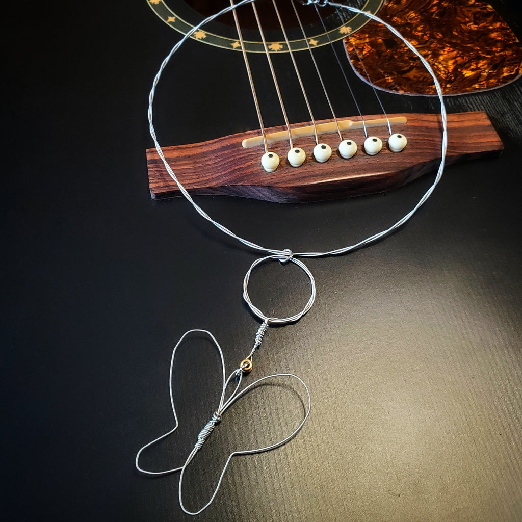 necklace with a butterfly style pendant made from upcycled guitar strings lying on the bridge of a black guitar.