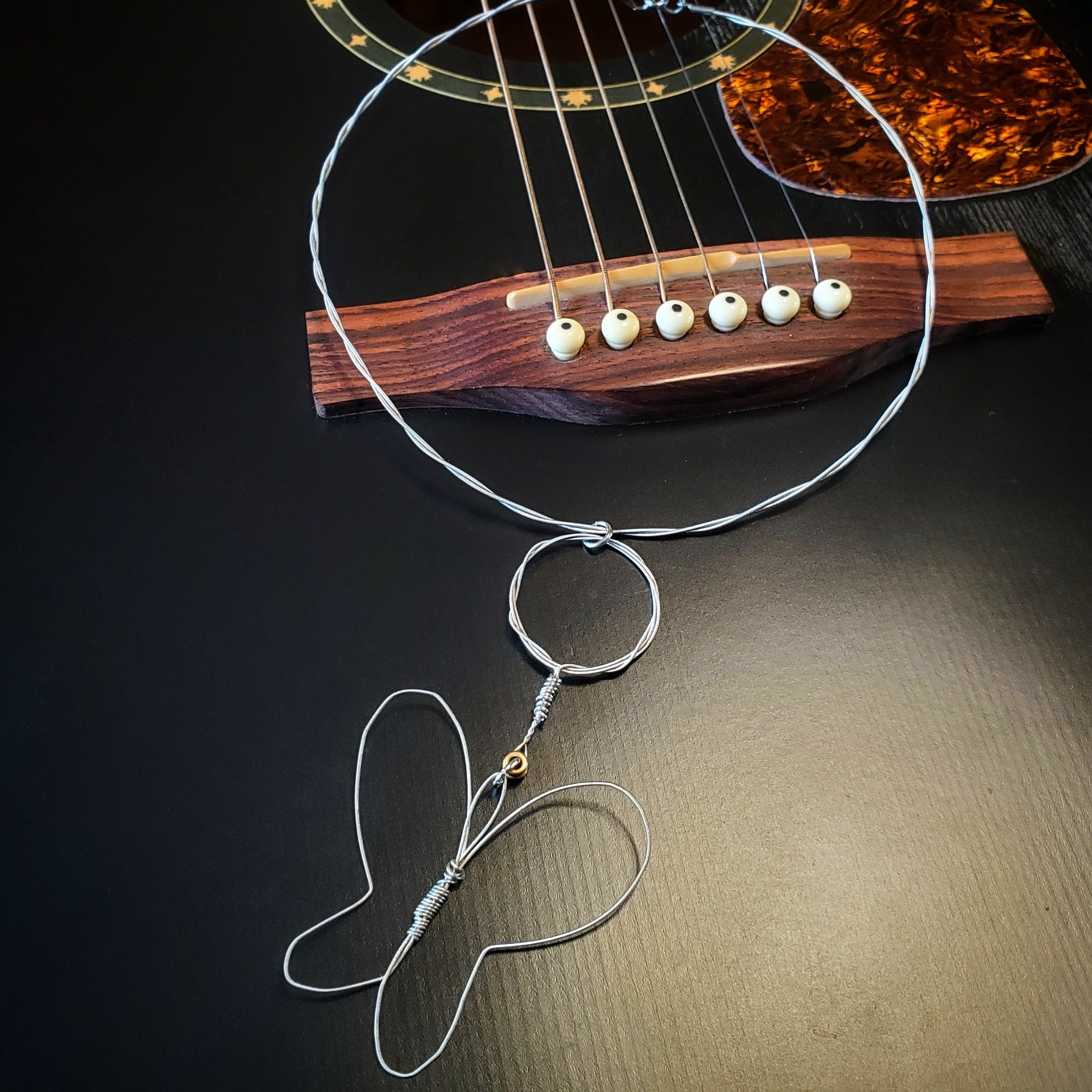 necklace with a butterfly style pendant made from upcycled guitar strings lying on the bridge of a black guitar.