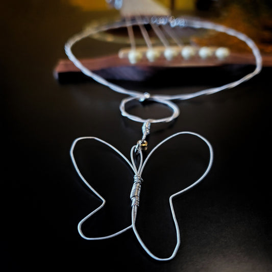 close-up of necklace with a butterfly style pendant made from upcycled guitar strings lying on the bridge of a black guitar