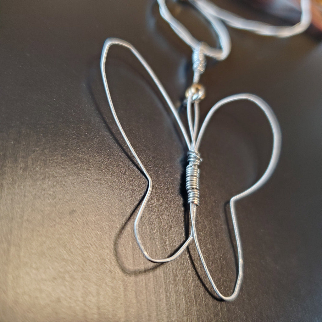 close-up of the pendant from a necklace with a butterfly style pendant made from upcycled guitar strings lying on a black background
