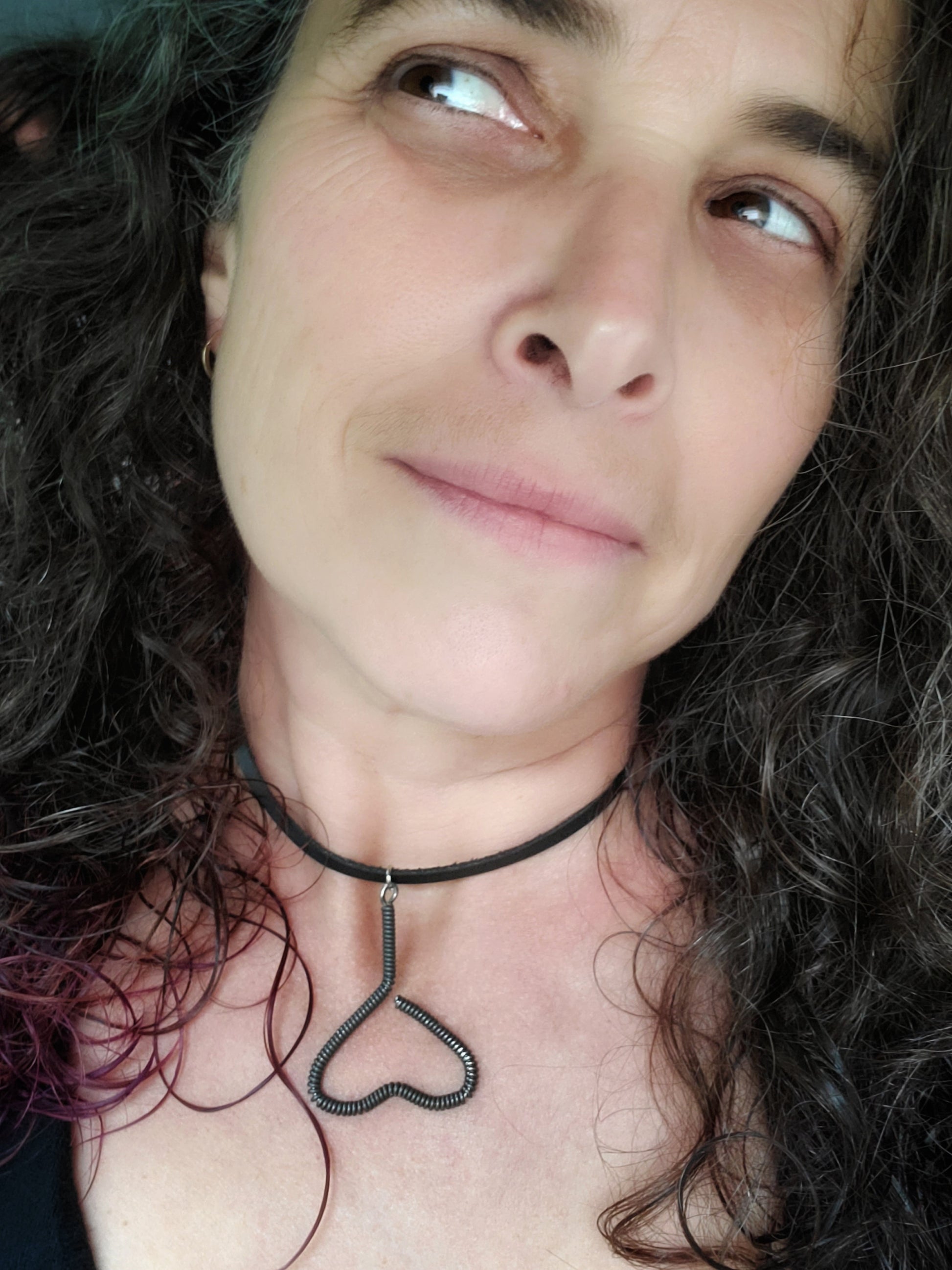 woman's head with black, grey and purple hair - she is wearing a necklace - pendant is in the shape of an upside down heart and is made from a black upcycled piano string - pendant hangs off a black leather cord
