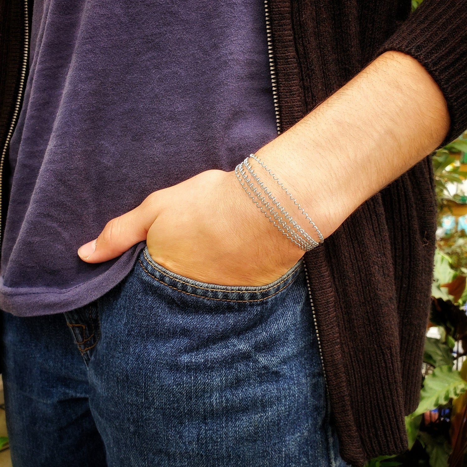 male body with the hand tucked into his jean's pocket - on the wrist he is wearing a silver coloured clasp style bracelet made from a series of upcycled snare drum strings 