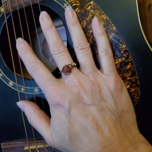 woman's hand lying on top of a black guitar- on her finger she is wearing a ing in the shape of a rose, made from an upcycled guitar string