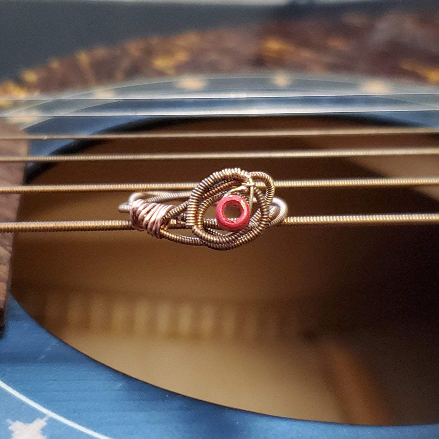 top view of a ing in the shape of a rose, made from an upcycled guitar string -ring is lying on top of a black guitar's strings