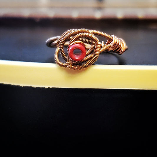 top view of a ring in the shape of a rose, made from an upcycled guitar string- the ring is lying on the body of a black guitar