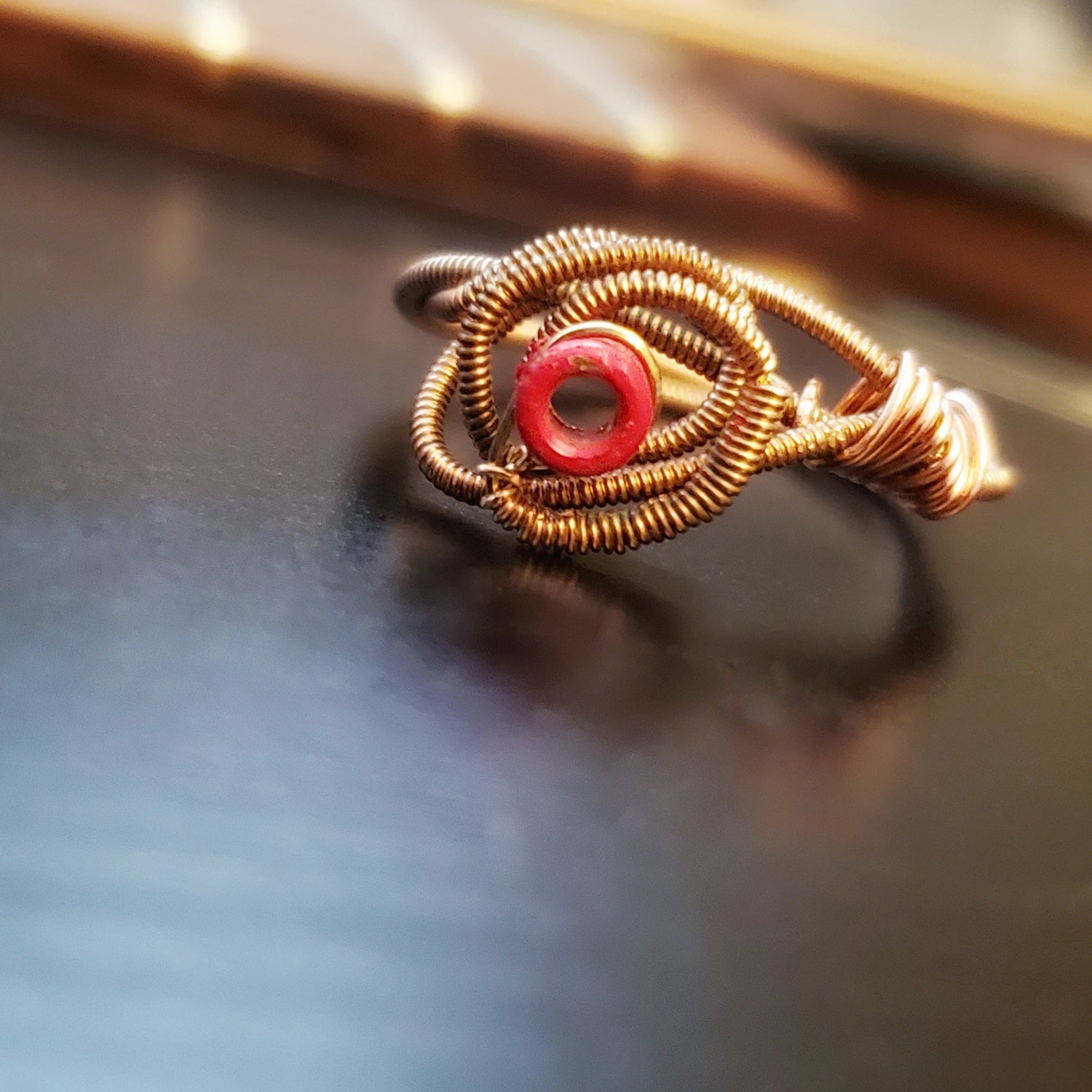 top view of a ing in the shape of a rose, made from an upcycled guitar string - ring is lying on top of the body of a black guitar
