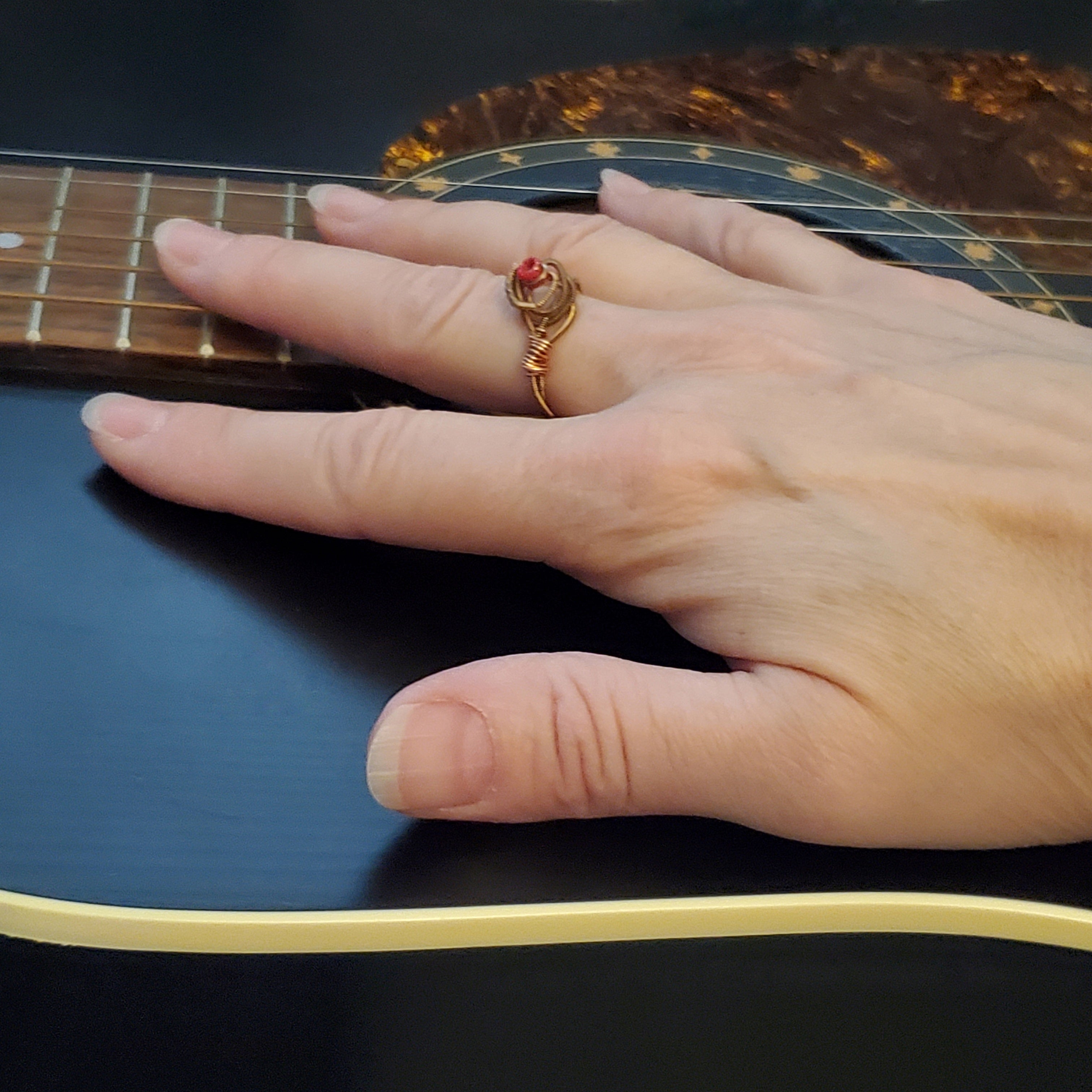 woman's hand lying on top of a black guitar- on her finger she is wearing a ing in the shape of a rose, made from an upcycled guitar string