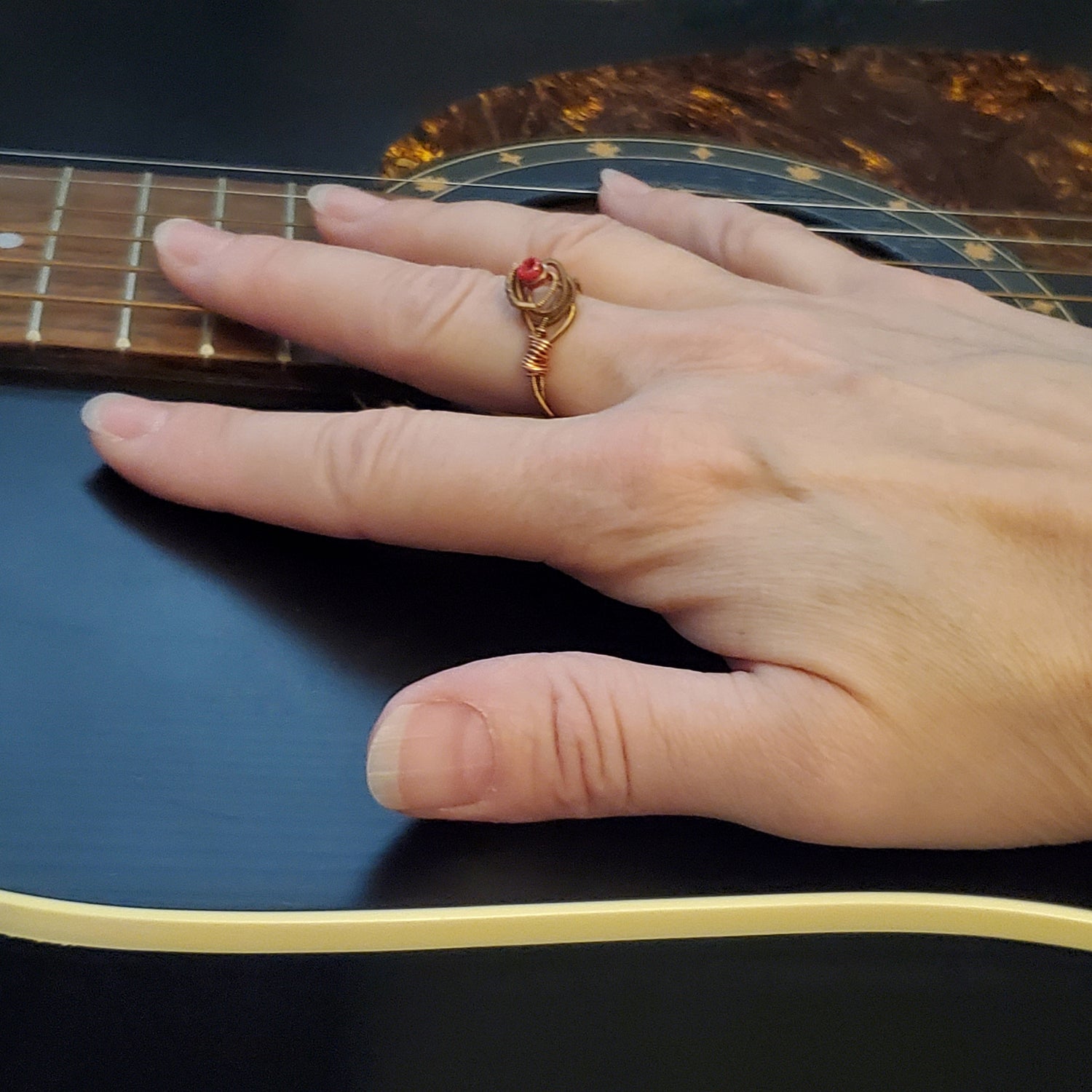 woman's hand lying on top of a black guitar- on her finger she is wearing a ing in the shape of a rose, made from an upcycled guitar string