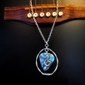 A necklace made from a blue marbled guitar pick and upcycled guitar strings with a silver coloured chain hangs in front of a black guitar