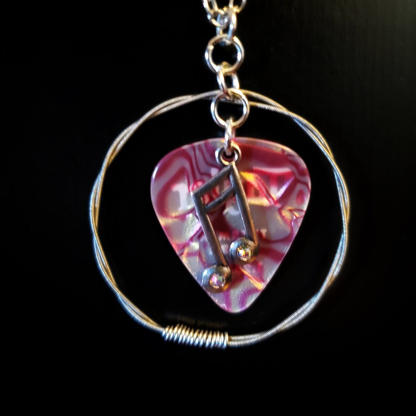 Close-up of a necklace made from a red marbled guitar pick and upcycled guitar strings with a silver coloured chain -black background