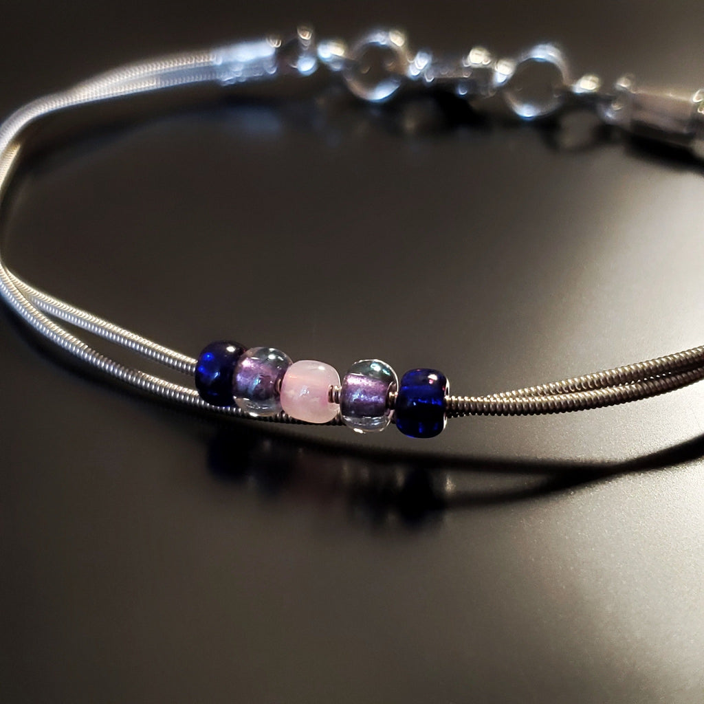 guitar string bracelet with blue, purple and pink bead representing the bisexual pride flag -black background