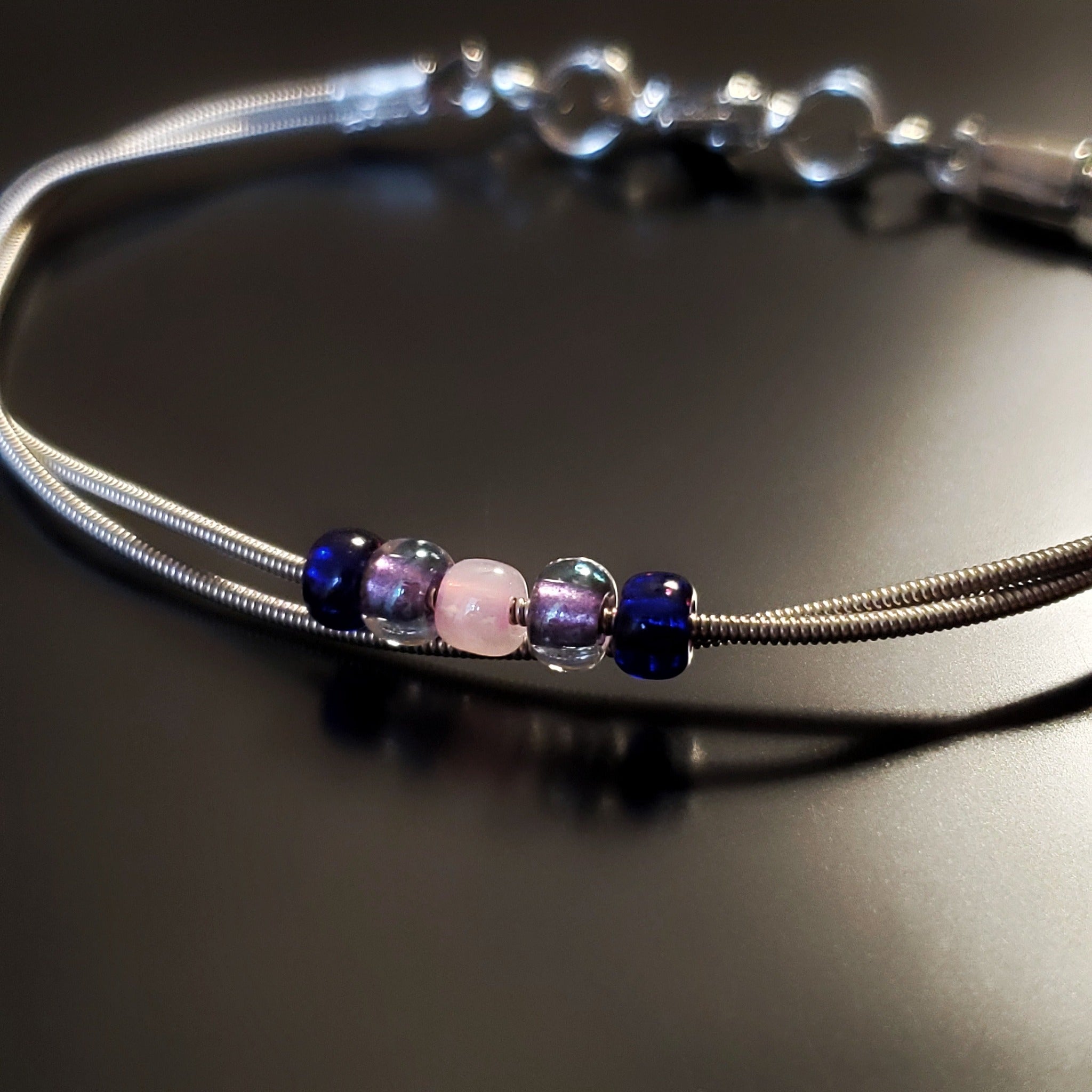 guitar string bracelet with blue, purple and pink bead representing the bisexual pride flag -black background