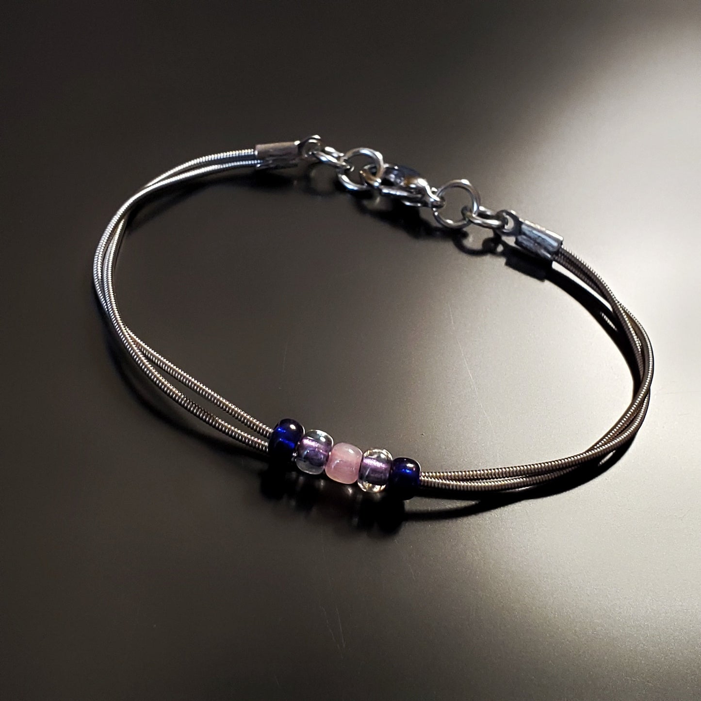 guitar string bracelet with blue, purple and pink bead representing the bisexual pride flag -black background