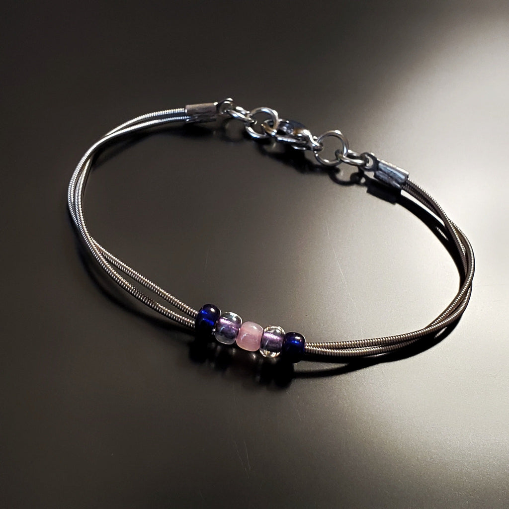 guitar string bracelet with blue, purple and pink bead representing the bisexual pride flag -black background