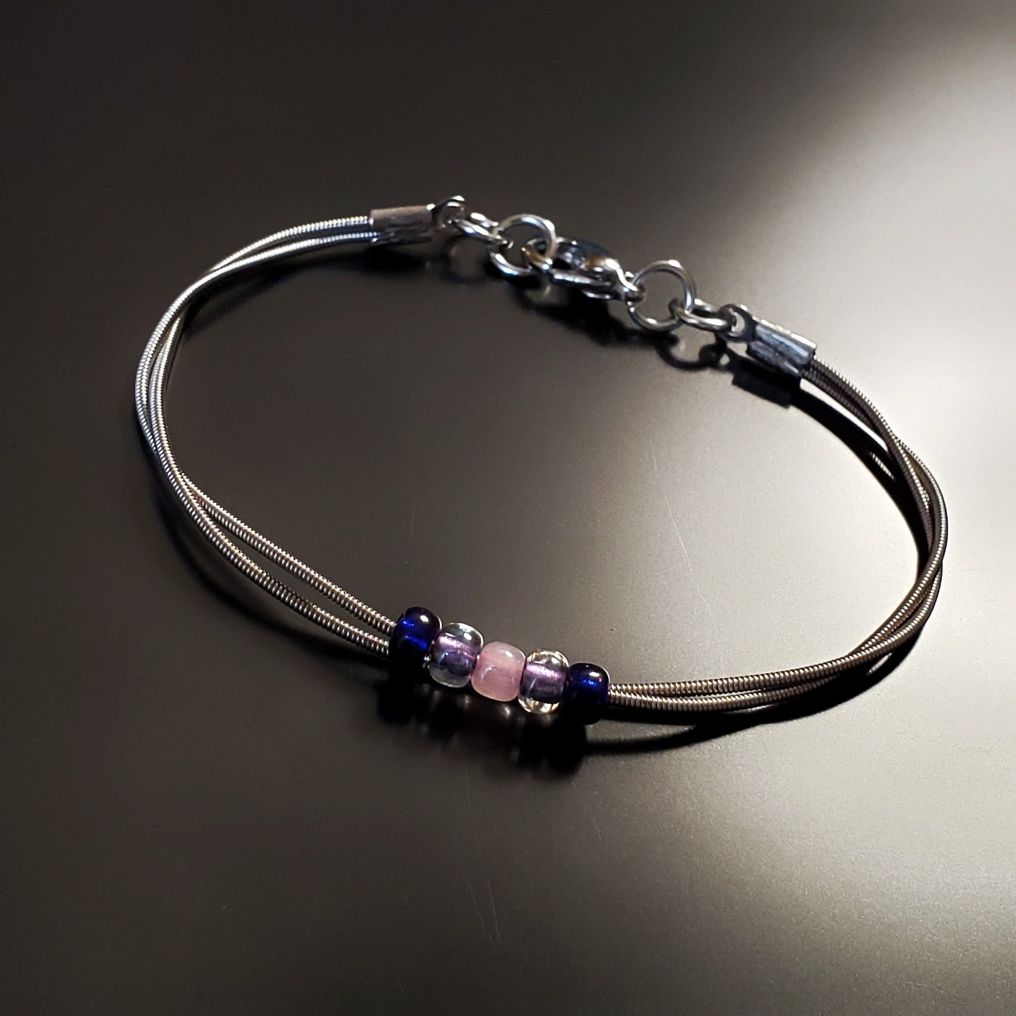 guitar string bracelet with blue, purple and pink bead representing the bisexual pride flag -black background