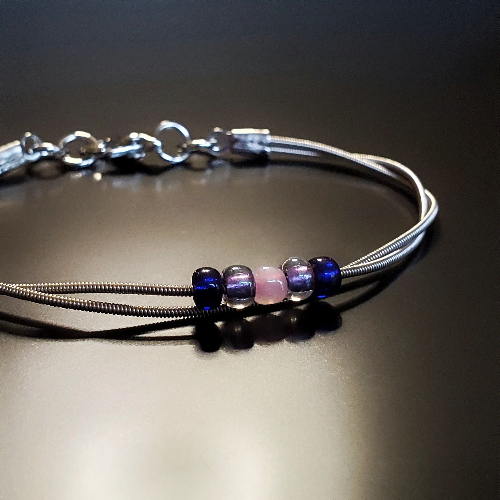 guitar string bracelet with blue, purple and pink bead representing the bisexual pride flag -black background