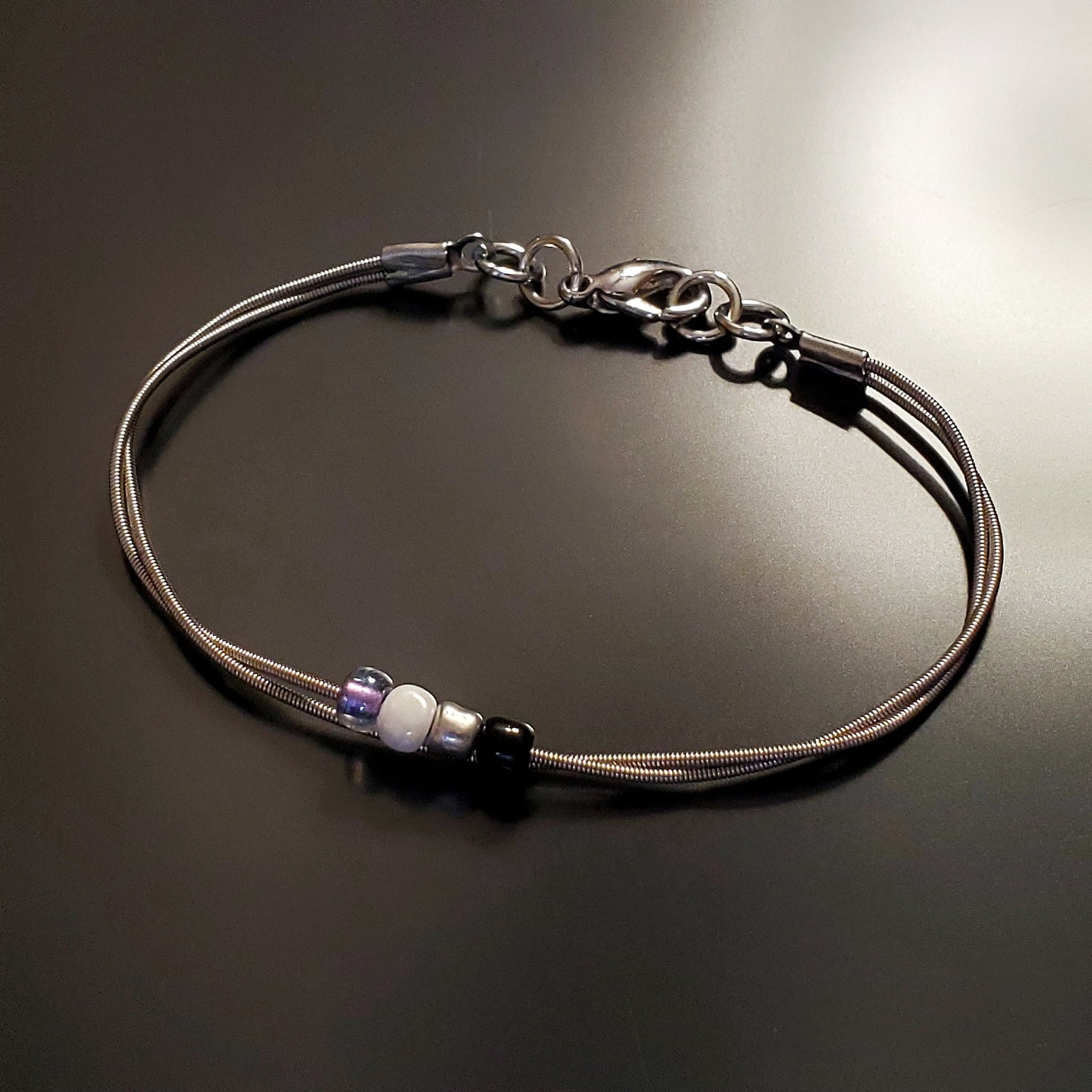 silver coloures clasp style bracelet with 4 glass beads representing the asexual pride flag (black, grey, white & purple) 