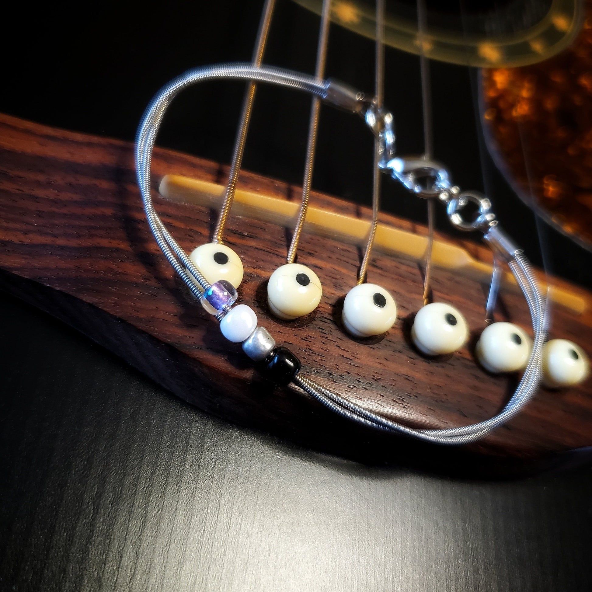 silver coloures clasp style bracelet with 4 glass beads representing the asexual pride flag (black, grey, white & purple) -bracelet is on the bridge of a black guitar