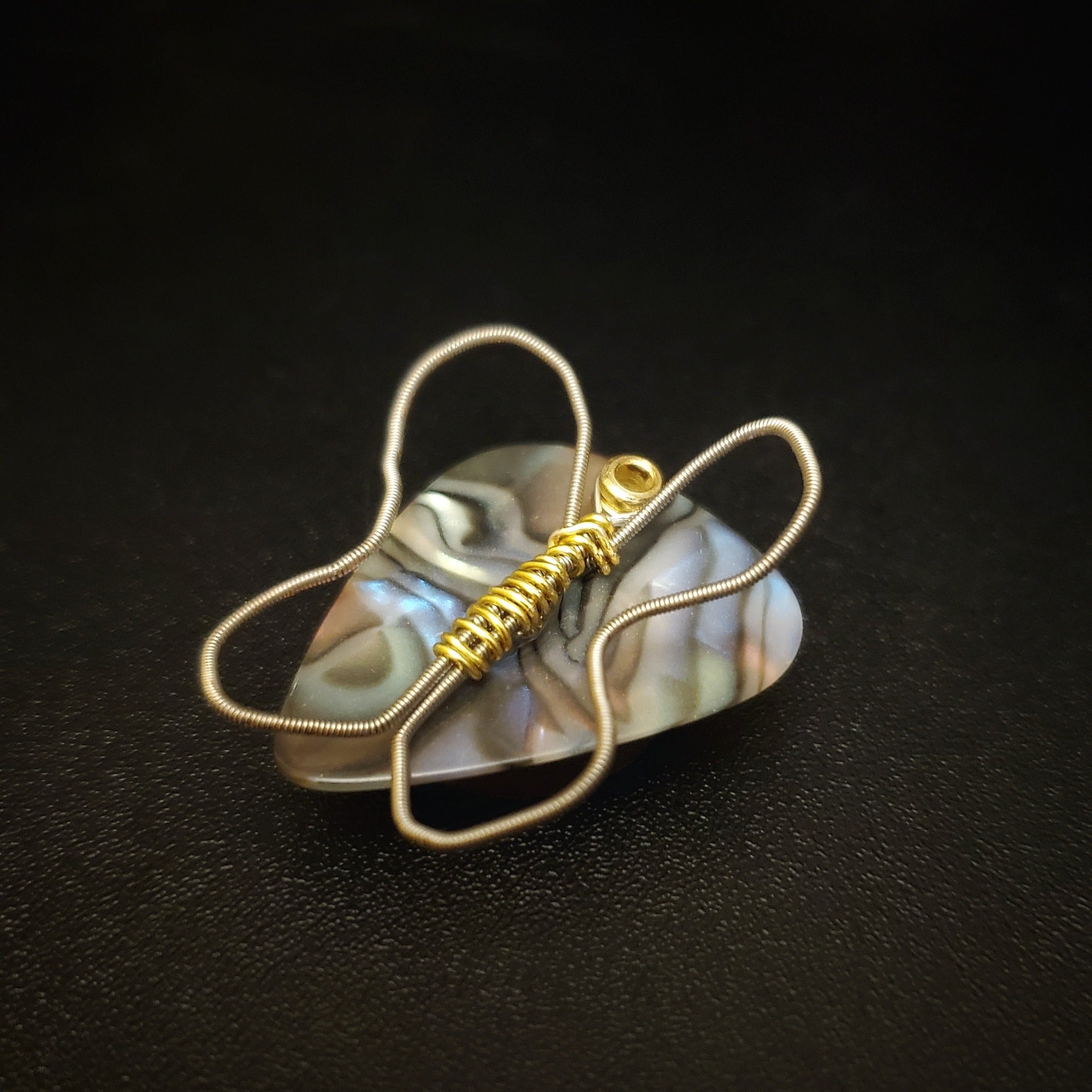 a magnet made from an upcycled guitar string shaped like a butterfly sitting on a multicoloured guitar pick - black background
