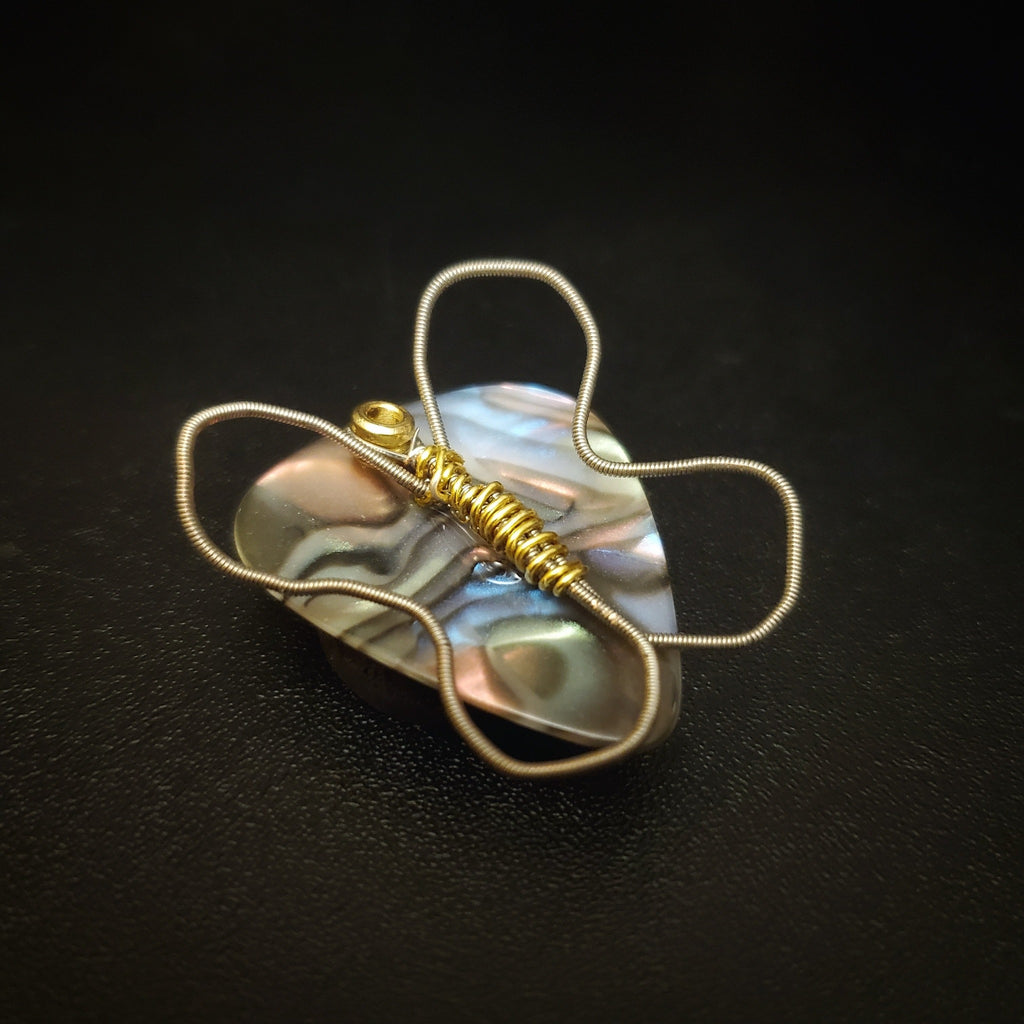 a magnet made from an upcycled guitar string shaped like a butterfly sitting on a multicoloured guitar pick - black background