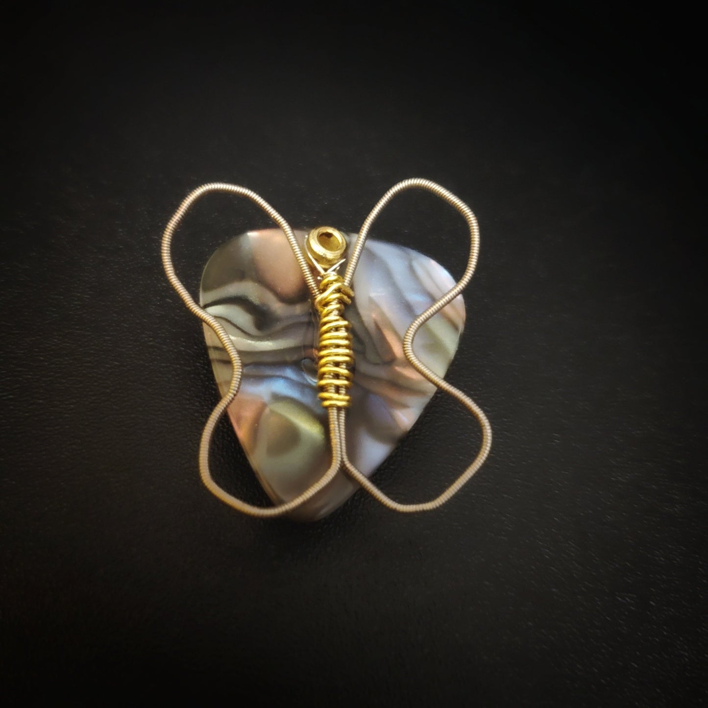 a magnet made from an upcycled guitar string shaped like a butterfly sitting on a multicoloured guitar pick - black background