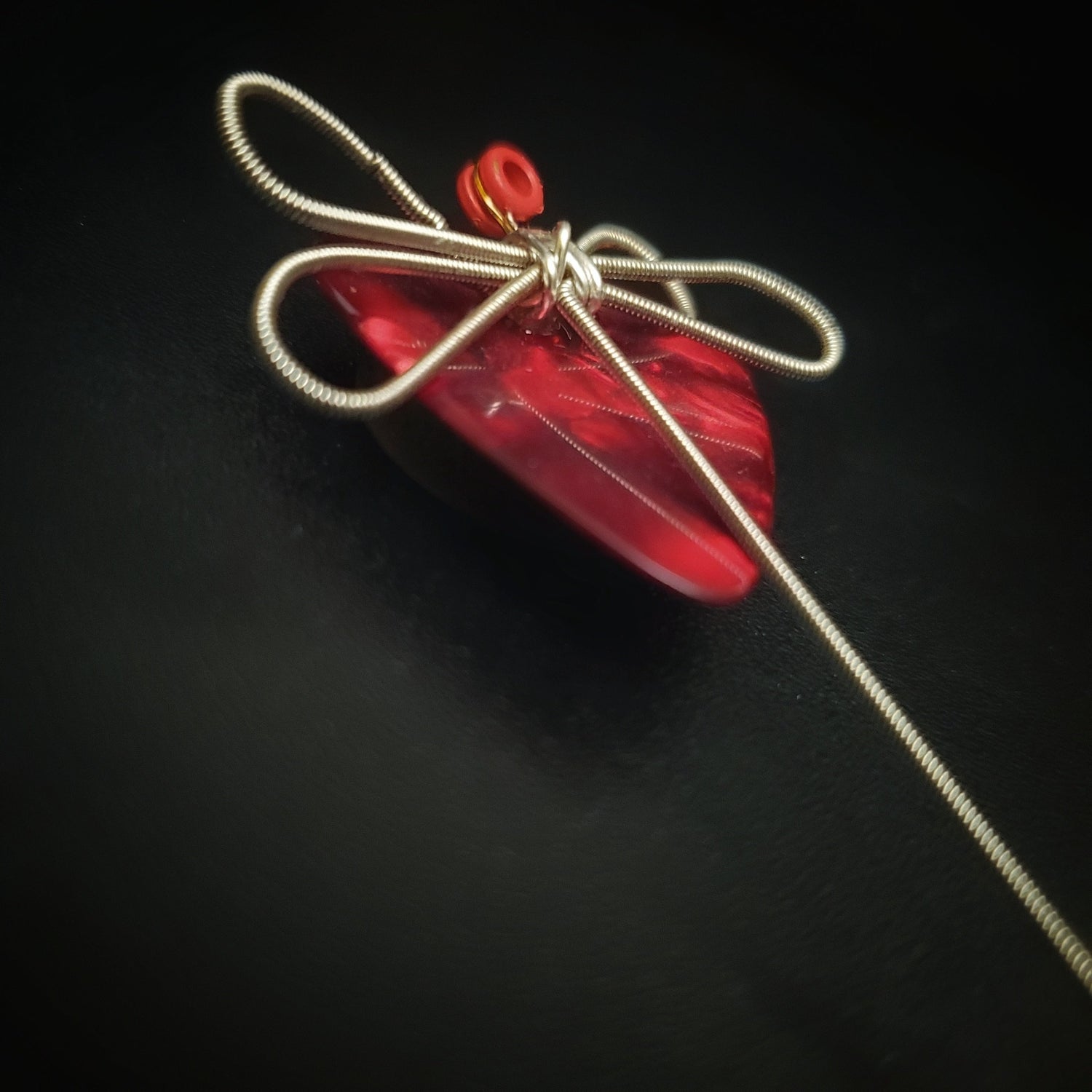 magnet made from an upcycled guitar string shaped like a dragonfly sitting on a dark red guitar pick - black background