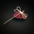 magnet made from an upcycled guitar string shaped like a dragonfly sitting on a dark red guitar pick - black background
