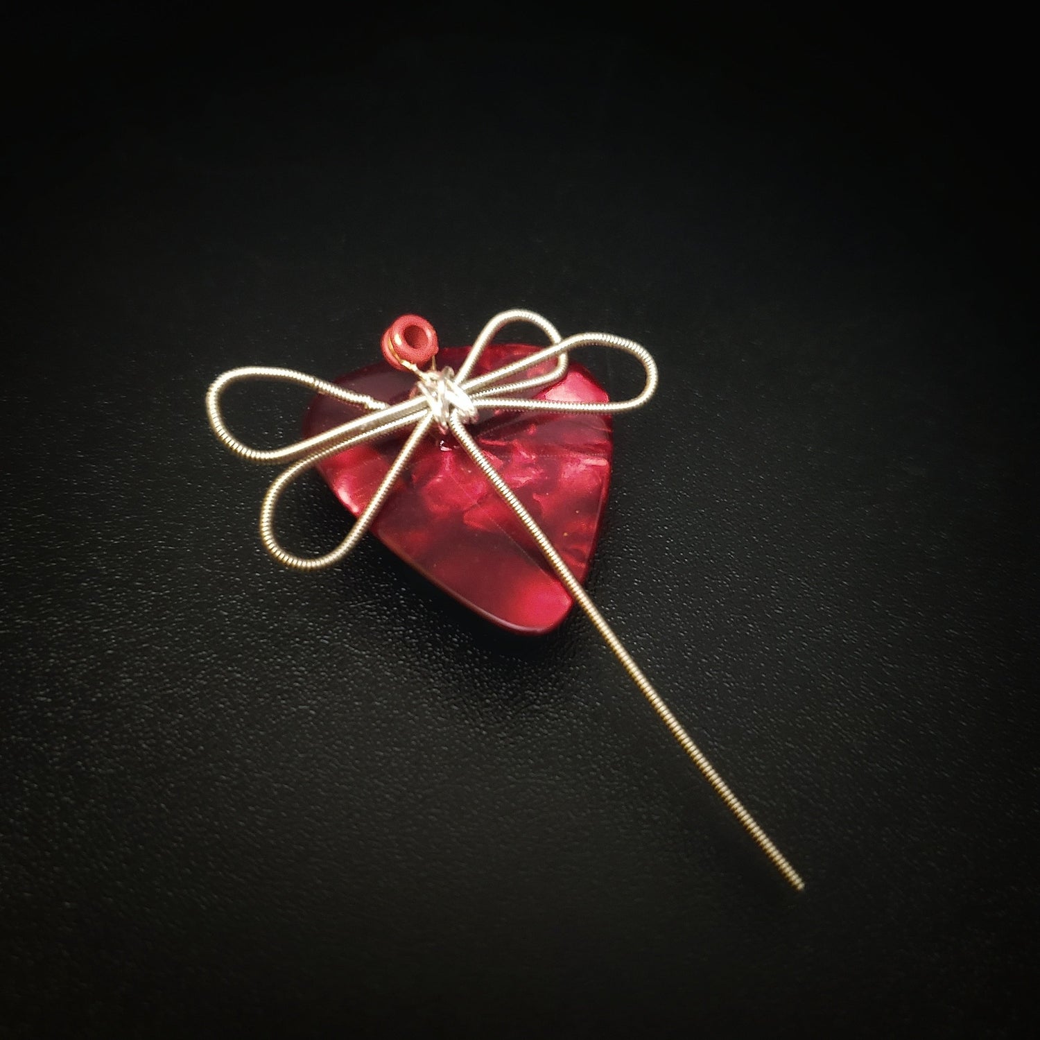 magnet made from an upcycled guitar string shaped like a dragonfly sitting on a dark red guitar pick - black background