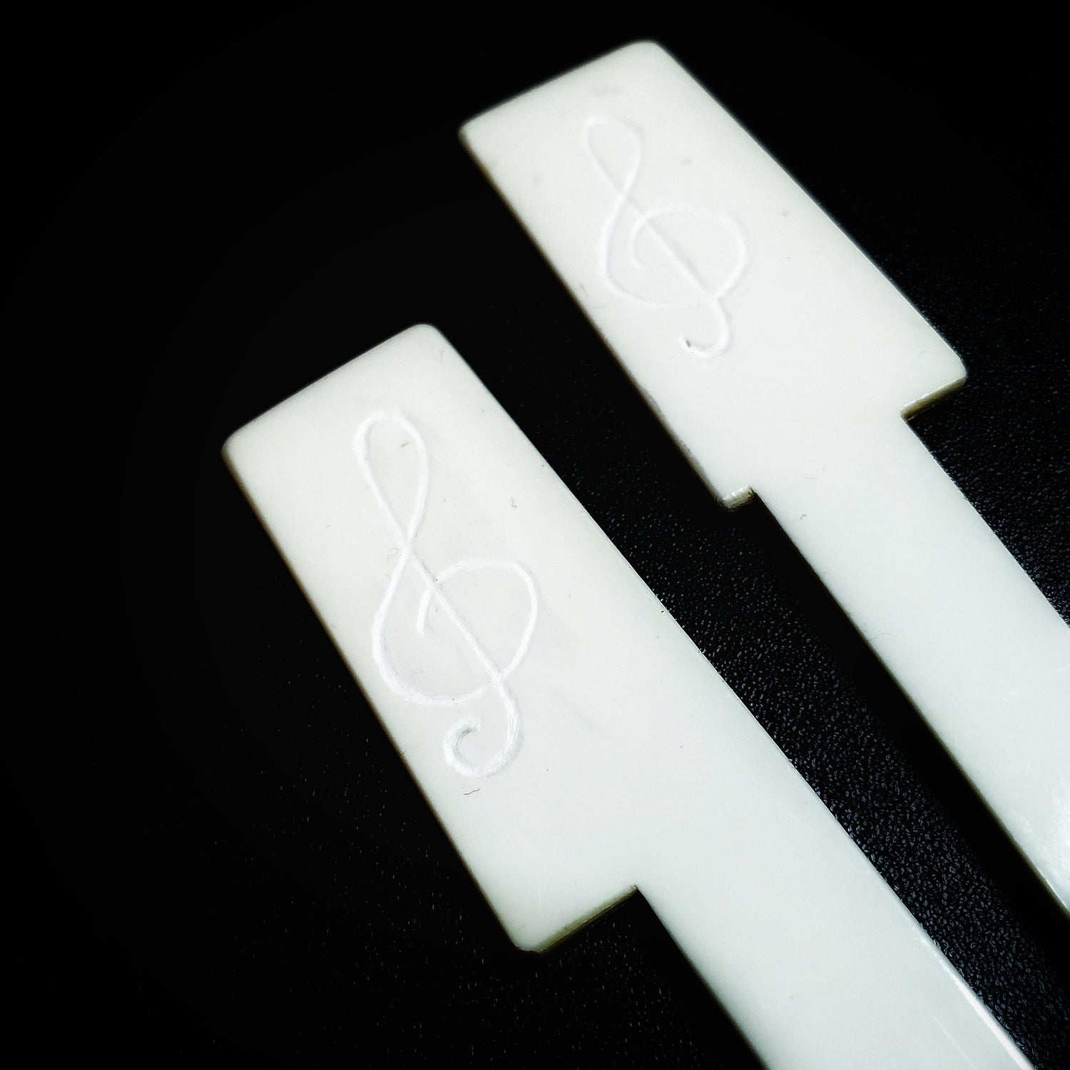 2 bookmarks made from white piano key topped -a treble clef has been etched on them