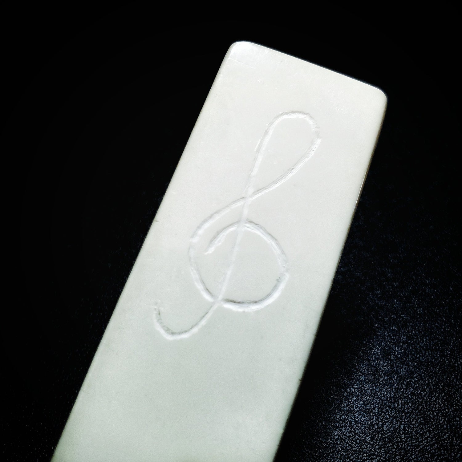 Close-up of a bookmark made from white piano key topper- a treble clef has been etched on it