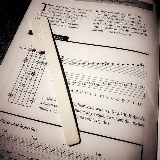 a white bookmark made from an upcycled piano key topper lies on top of a white page with black music notes and writing